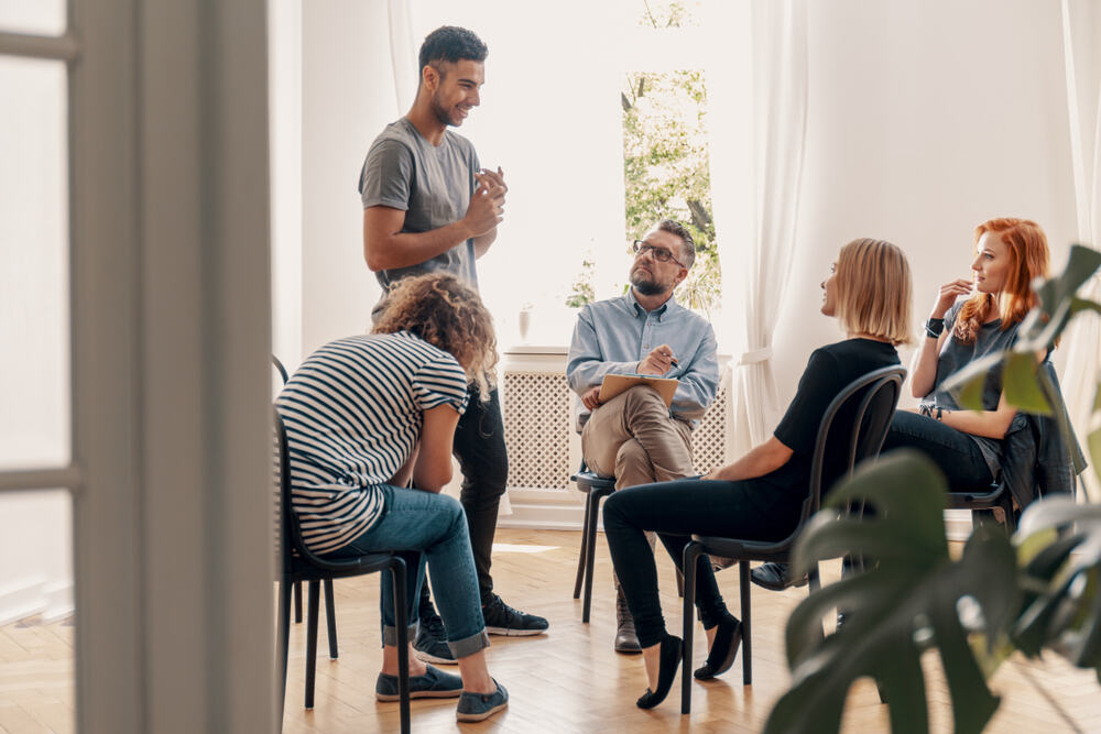 A man standing and talking in group therapy. 