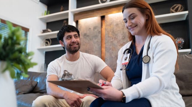 Smiling healthcare professional with stethoscope talking with a patient and taking notes on a clipboard