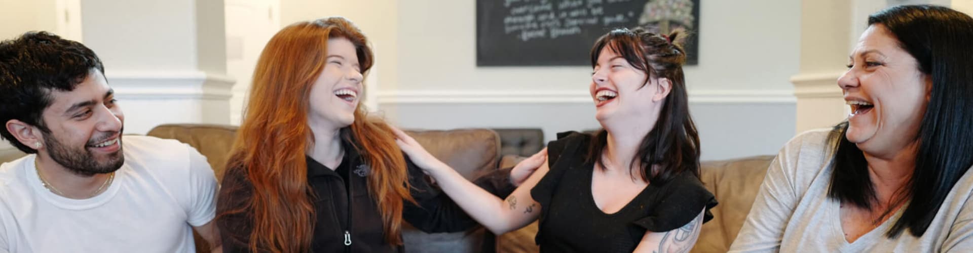 Four people sitting on a couch smiling and laughing together, showing a warm and friendly atmosphere