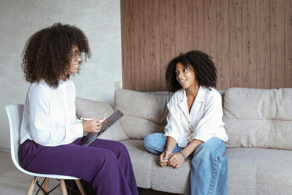 Therapist sitting with a tablet and smiling while speaking with a client seated on a couch during a counseling session.