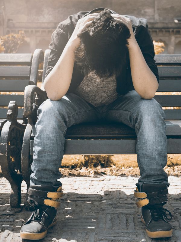 a man sitting on a bench and holding his head in his hands